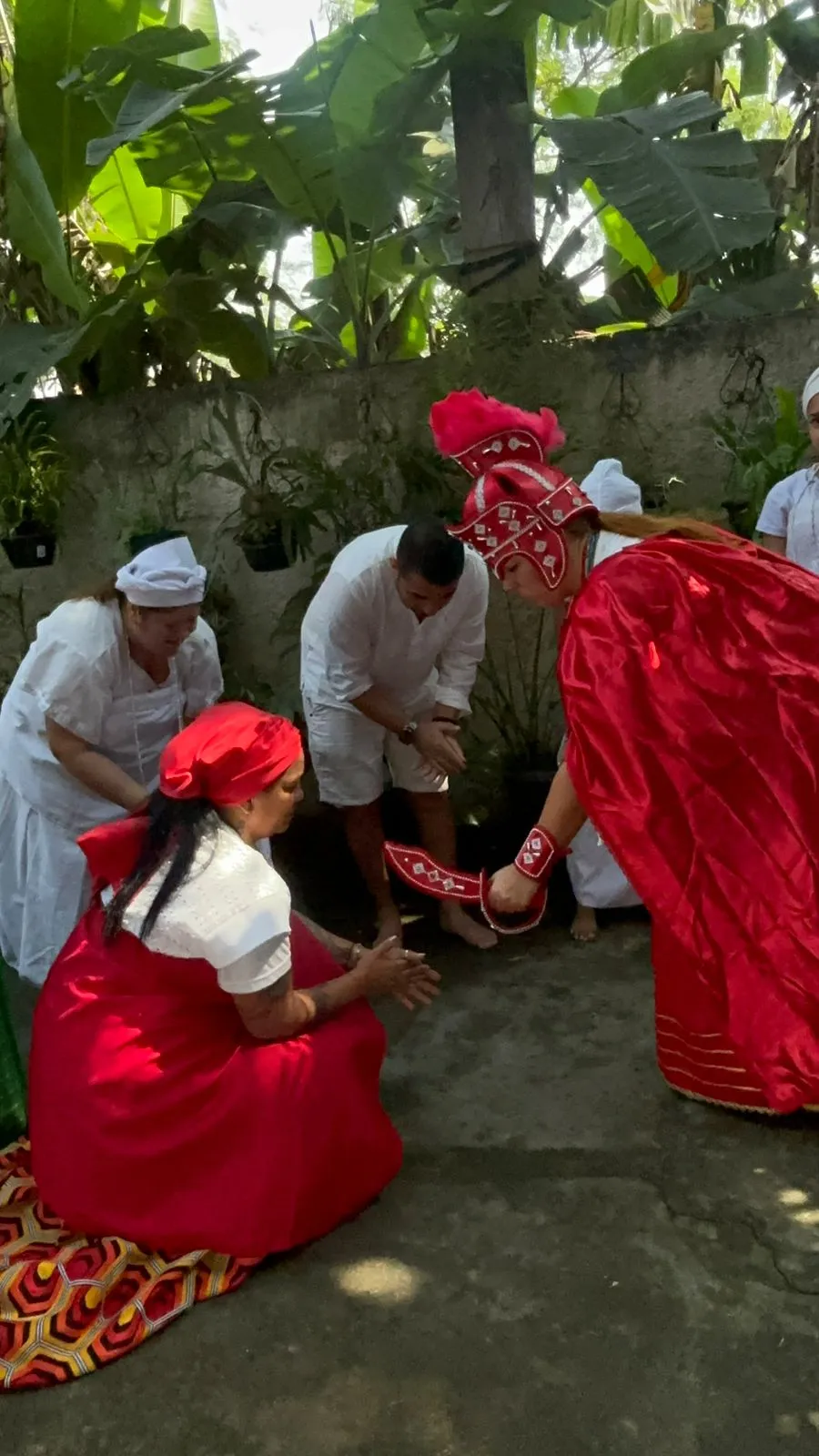 Médiuns com roupas de baiana vermelhas saudando os filhos da casa no quintal do templo