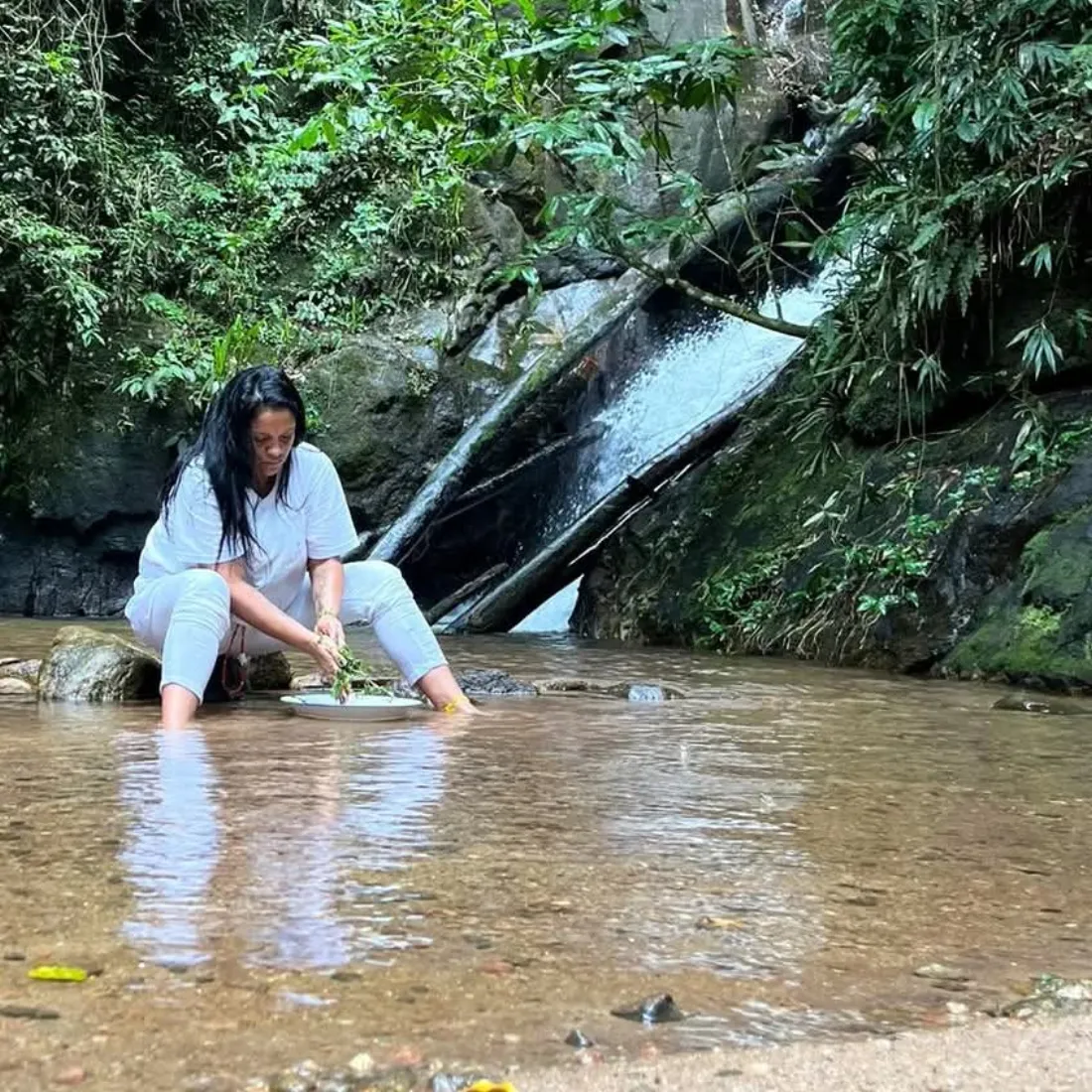 Bruxa Lorena agachada na água da cachoeira preparando uma oferenda