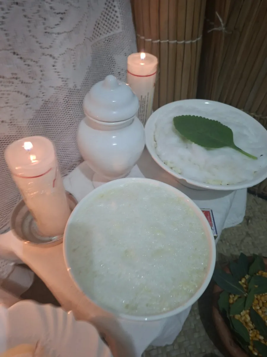 Tigela de canjica branca, vela acesa e folha sobre o prato no altar