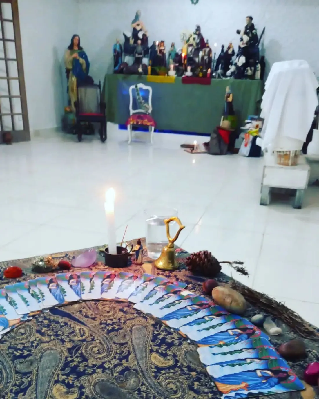 Cartas do Baralho Cigano abertas em leque sobre um pano estampado, com vela e sino