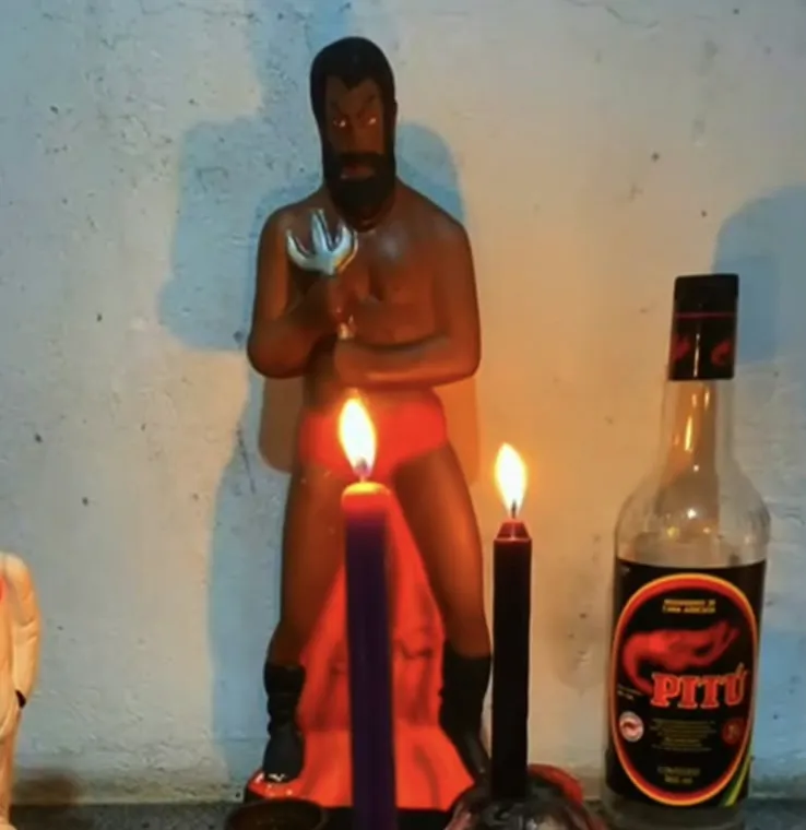 Imagem de Exu no altar com velas acesas e garrafa, guardião da casa
