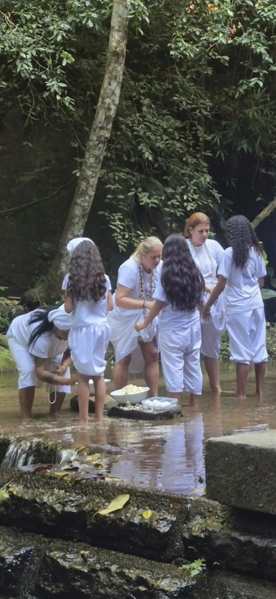 Médiuns de branco com os pés na água do rio durante a gira