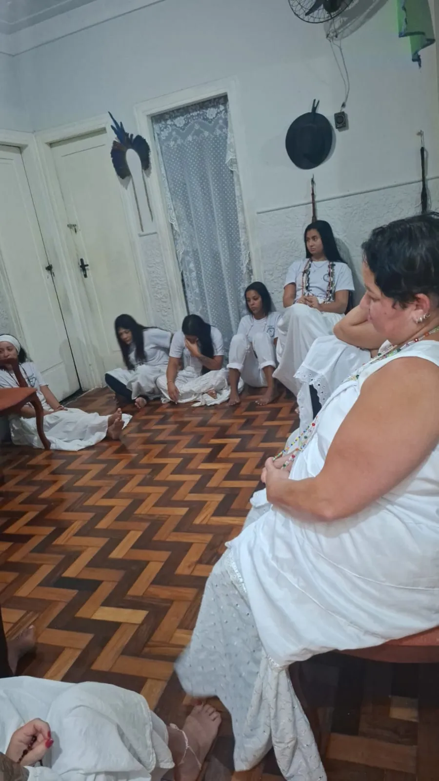 Médiuns de branco sentados no chão de taco do templo em concentração