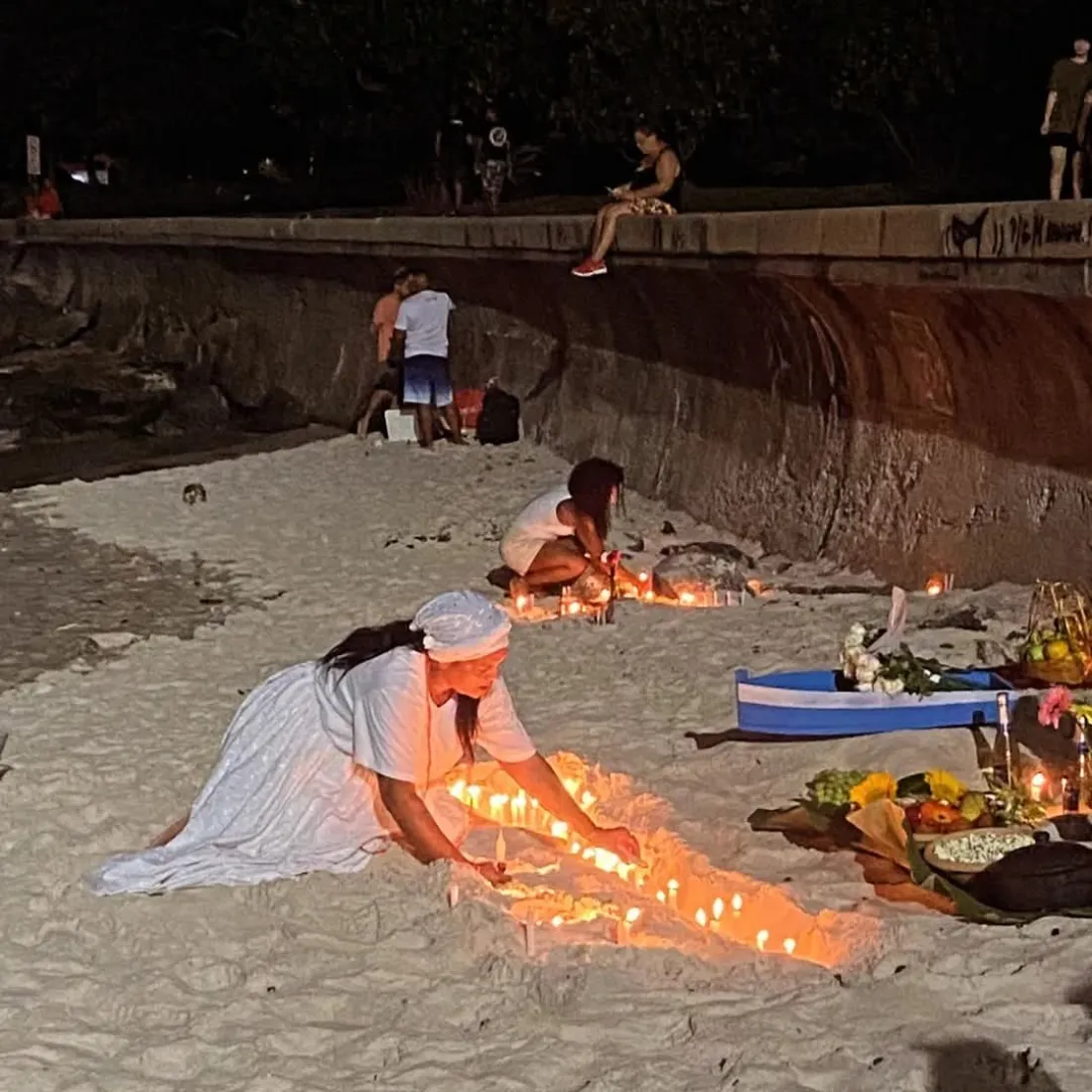 Oferenda com velas acesas na areia da praia, à noite