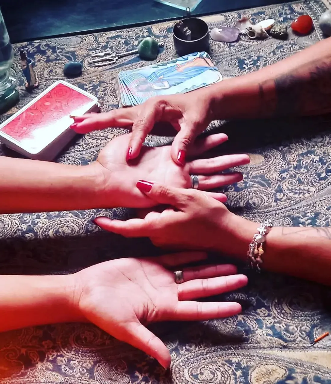 Mãos abertas sobre a mesa durante uma leitura de quiromancia, com cartas e cristais ao redor