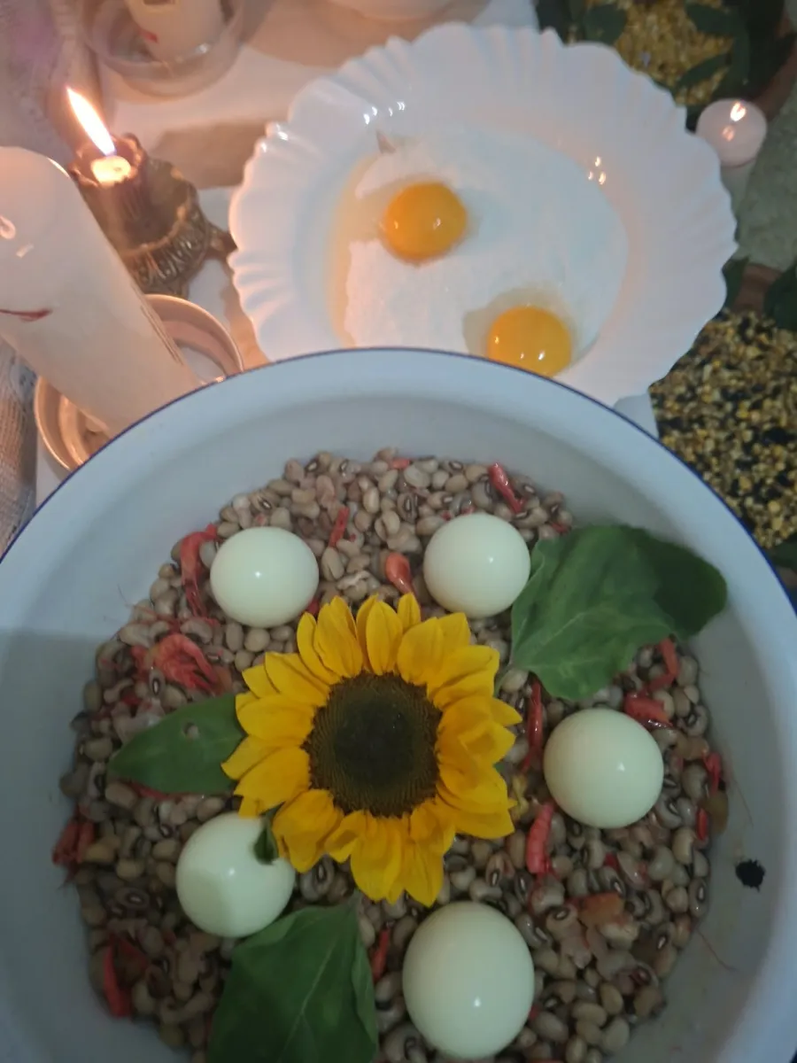 Oferenda com girassol, ovos e grãos numa bacia, com velas acesas