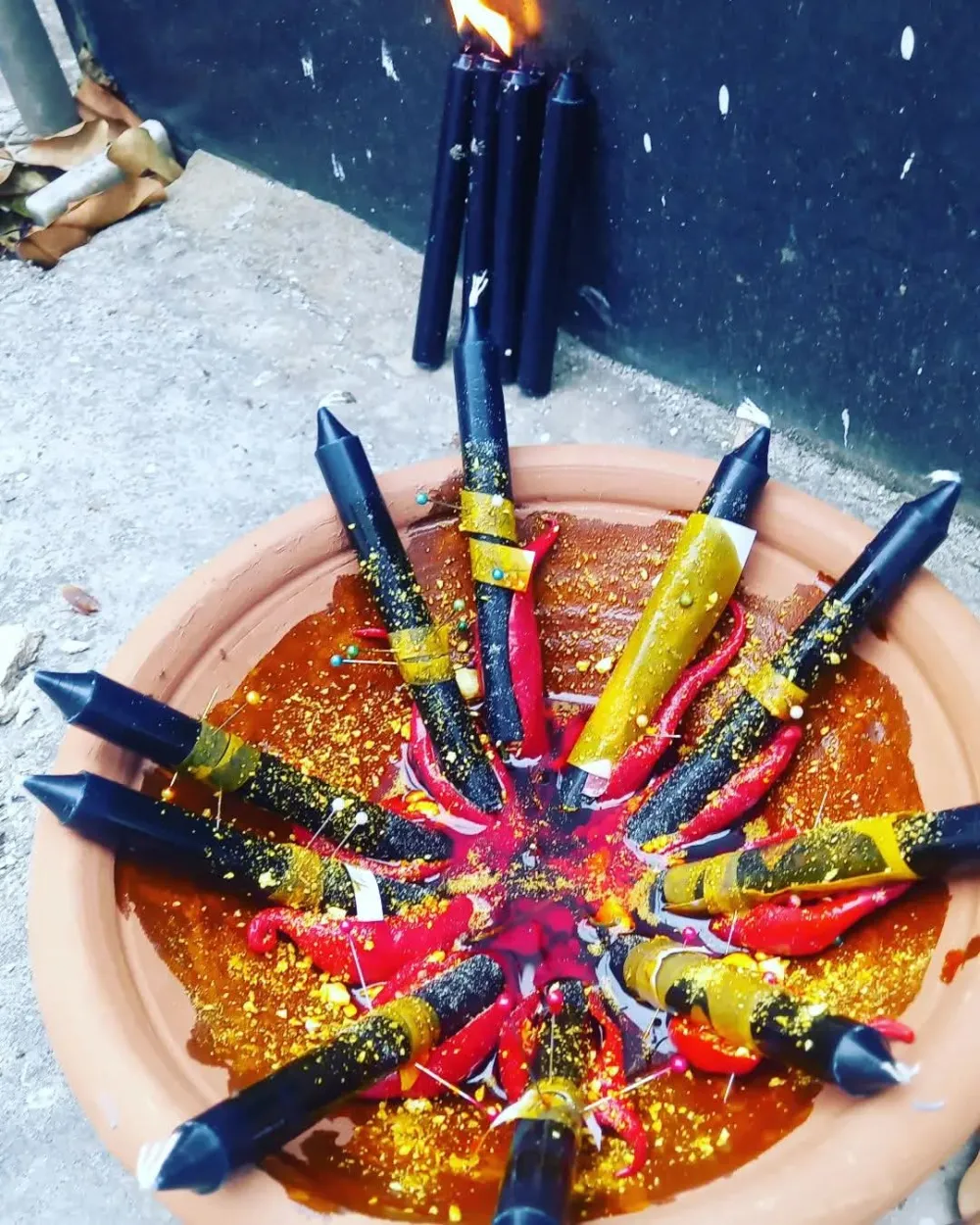 Velas pretas, vermelhas e amarelas dispostas em estrela sobre um alguidar de barro